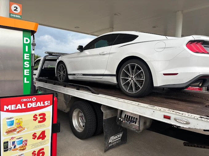 White sports car secured on the SOS Towing flatbed at a fuel stop