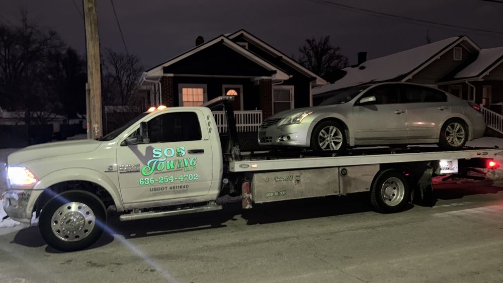 SOS Towing LLC flatbed tow truck loaded with a sedan on a snowy Alton street at night